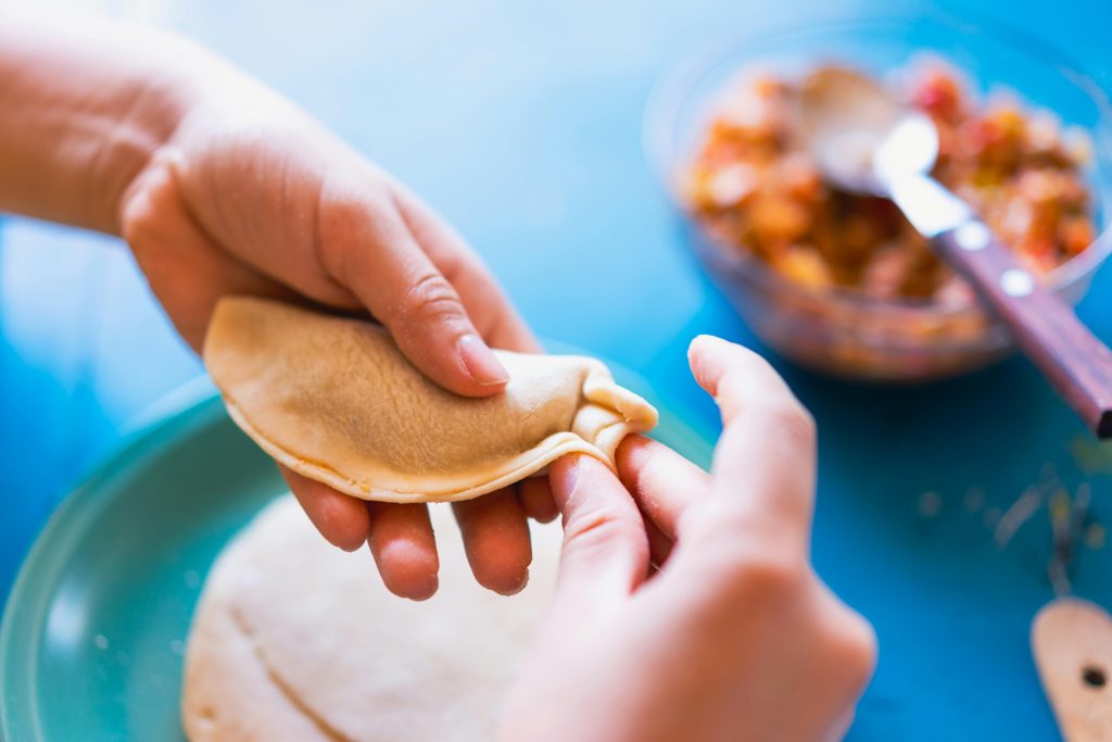 Hands folding empanadas dough with colorful filling in the kitchen.